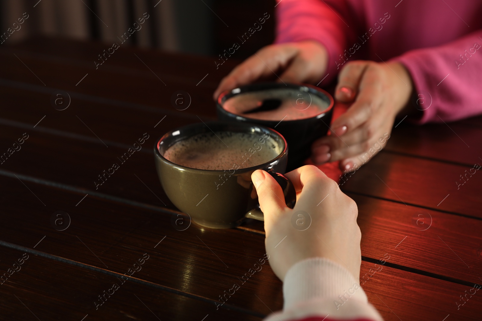 Photo of Women with cups of hot coffee at wooden table, closeup