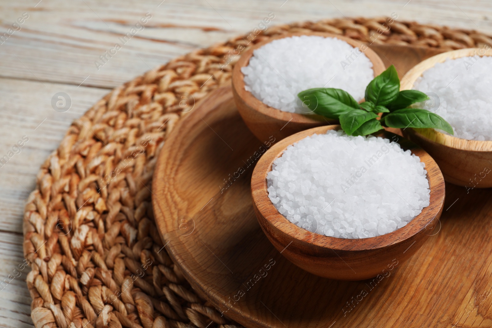 Photo of Bowls of natural sea salt on white wooden table, space for text