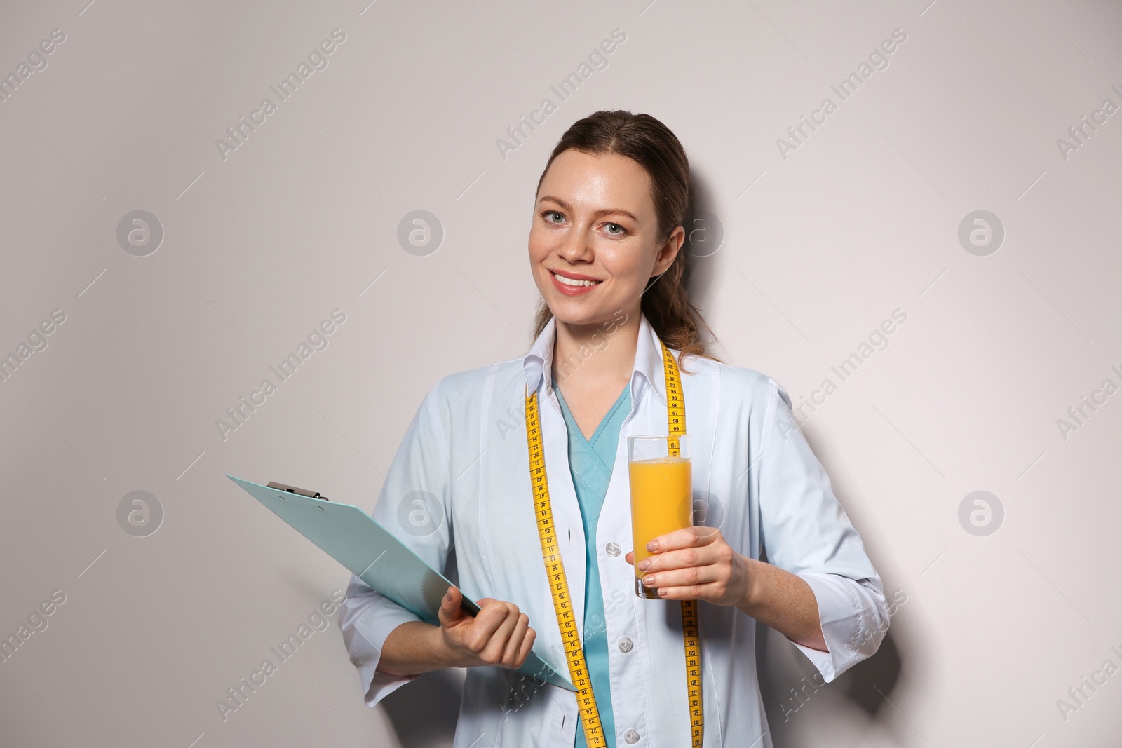 Photo of Nutritionist with glass of juice and clipboard on light grey background