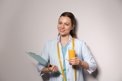 Nutritionist with glass of juice and clipboard on light grey background