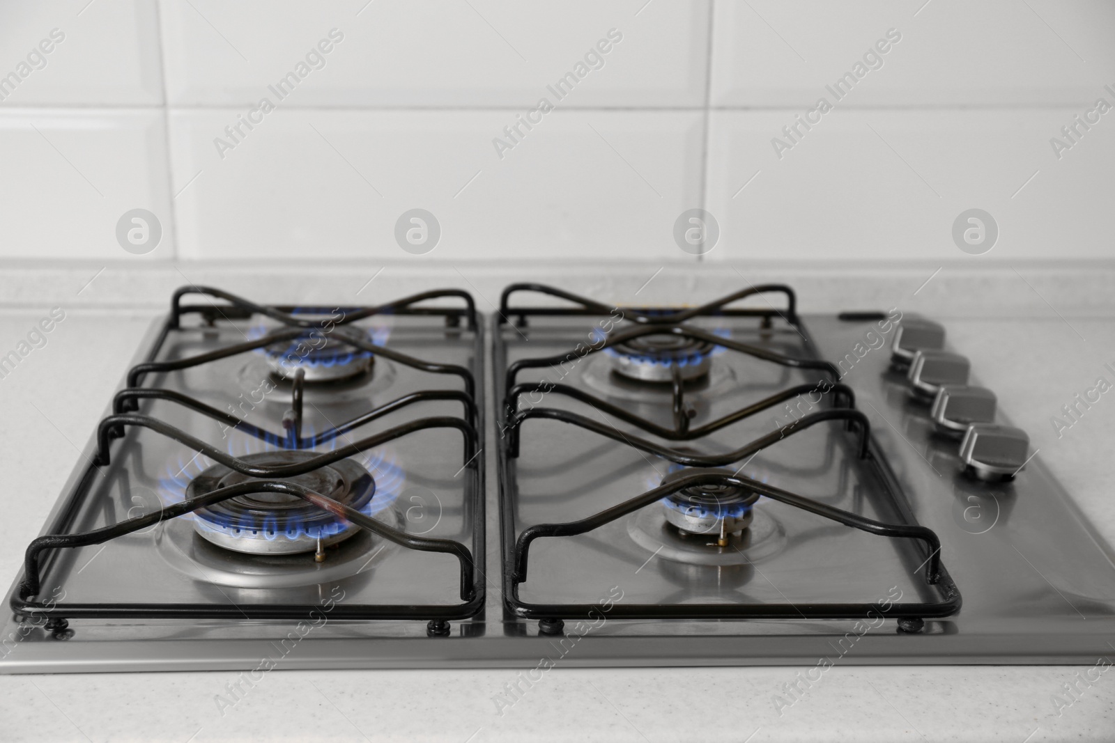 Photo of Gas cooktop with burning blue flames in kitchen