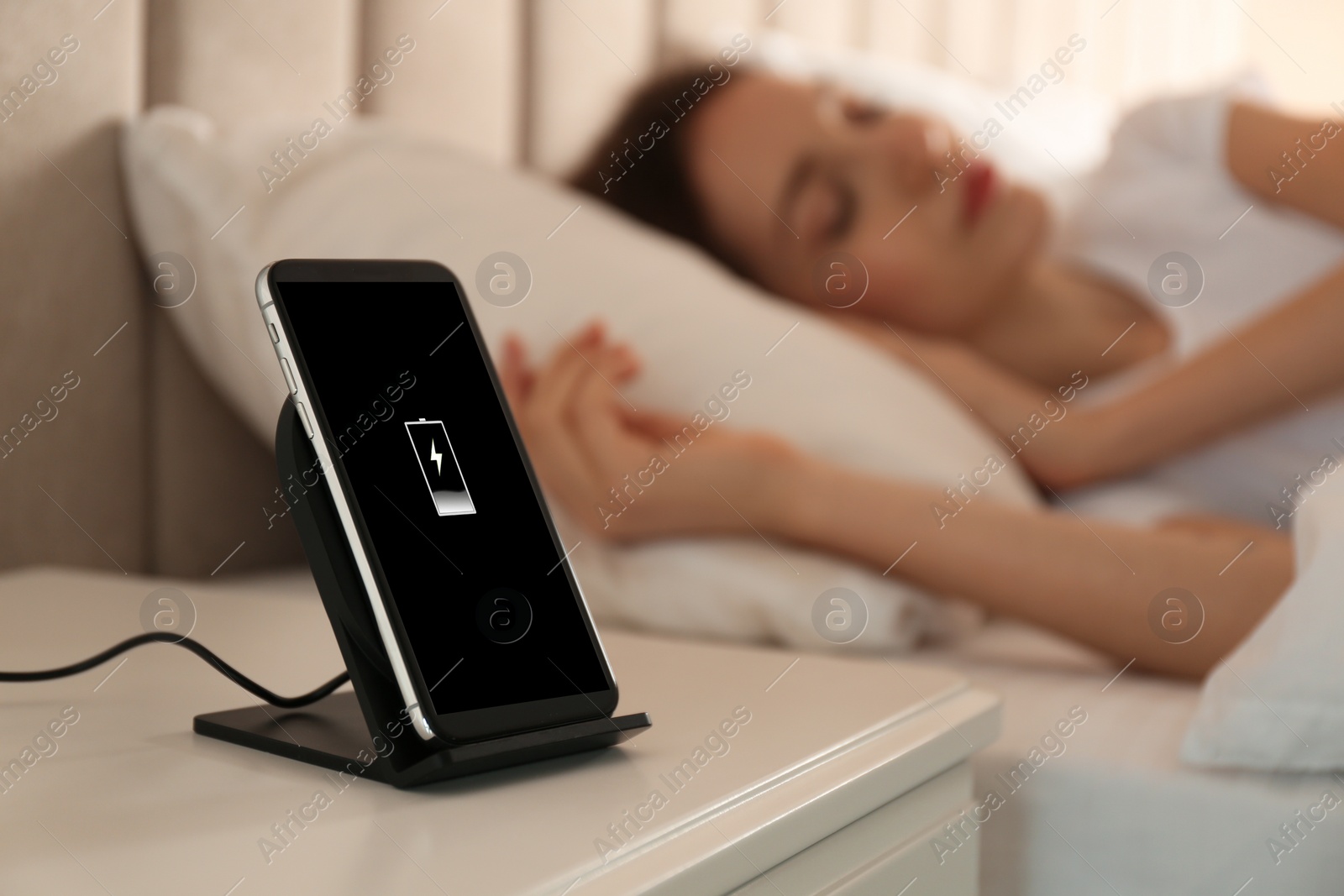 Photo of Smartphone charging on wireless pad and woman sleeping in bed