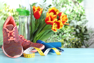 Photo of Composition with spring flowers and sports items on light blue wooden table against blurred greenery