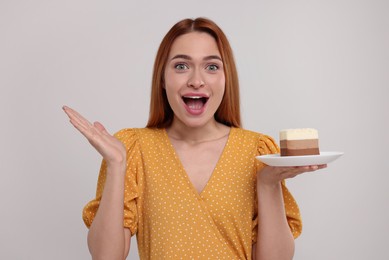 Emotional young woman with piece of tasty cake on light grey background