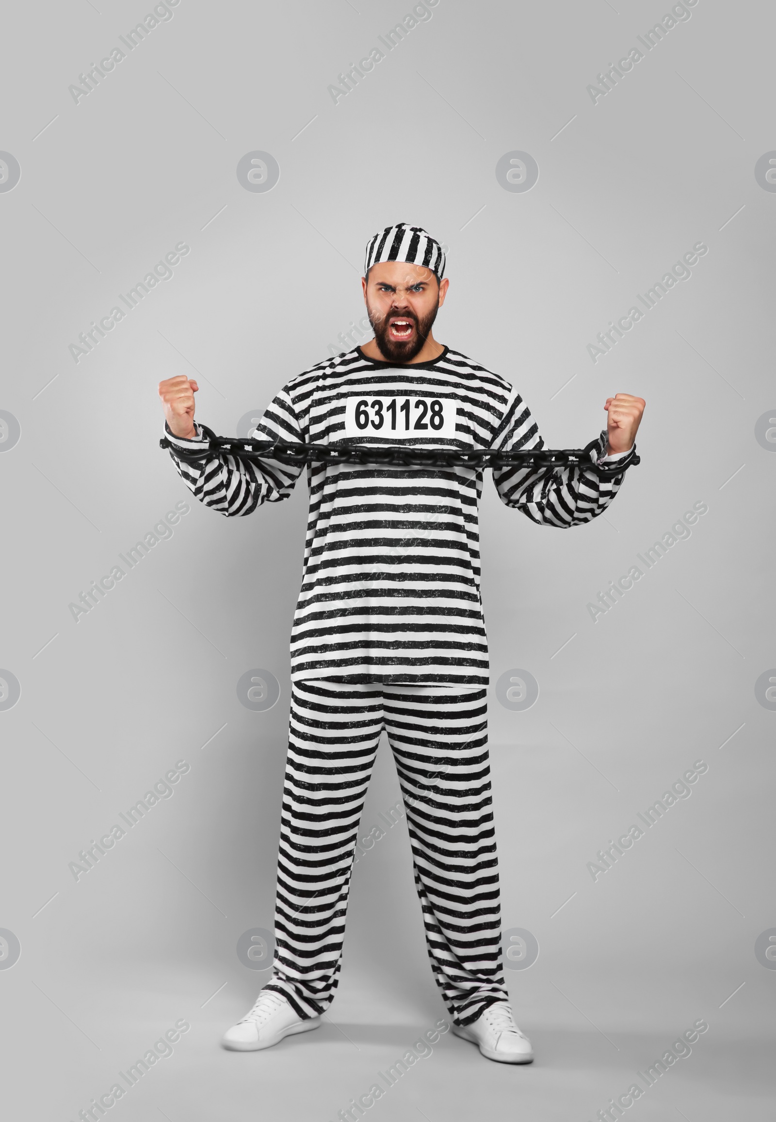 Photo of Emotional prisoner in special uniform with chained hands on grey background