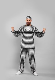 Emotional prisoner in special uniform with chained hands on grey background