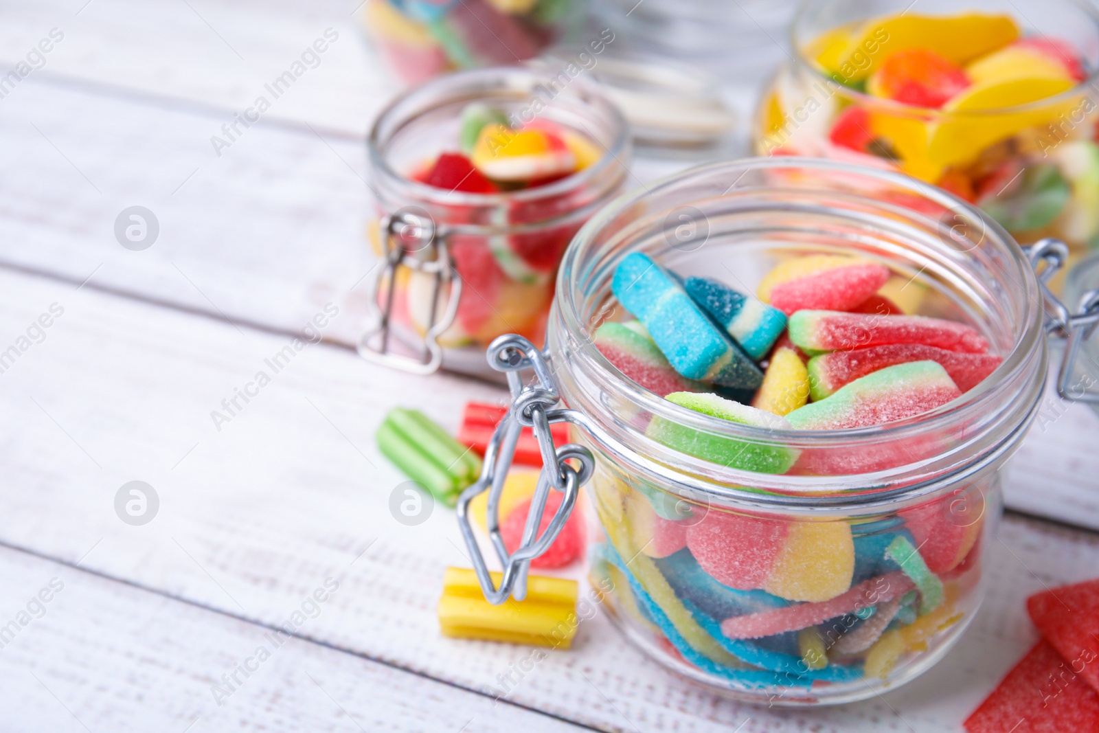 Photo of Tasty jelly candies in different jars on white wooden table, space for text