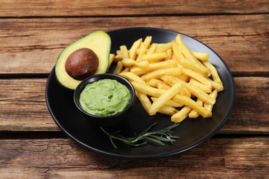 Photo of Plate with french fries, guacamole dip and avocado served on wooden table
