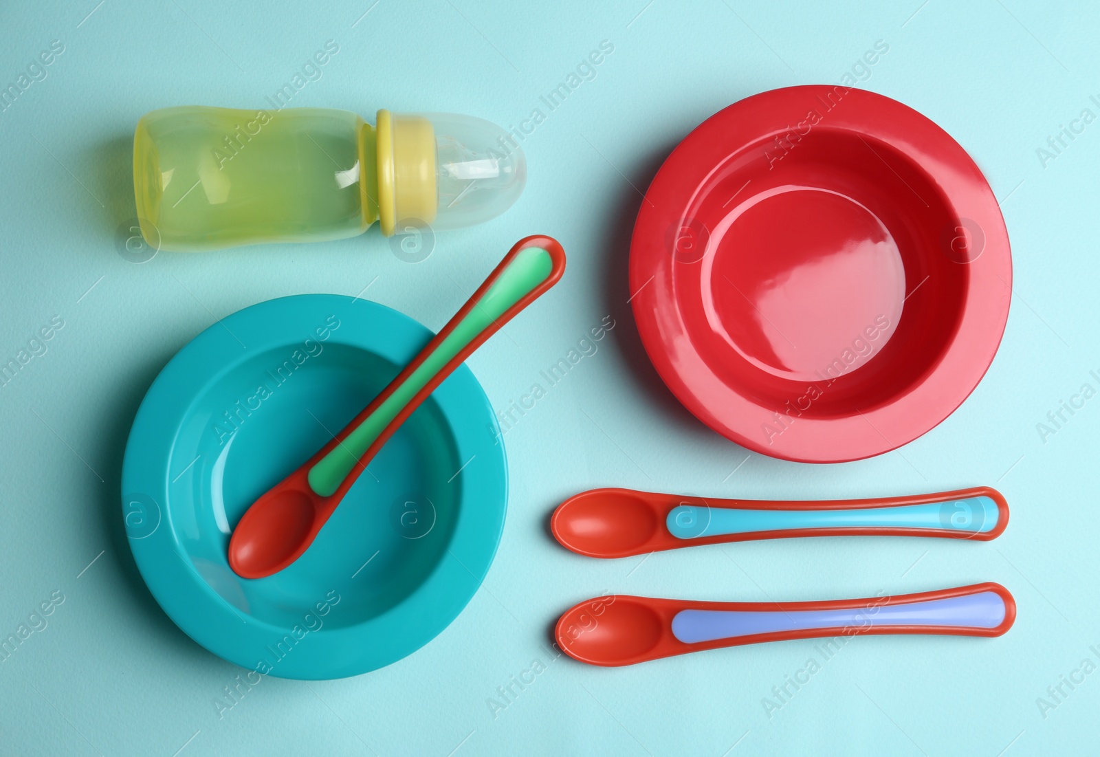 Photo of Set of colorful plastic dishware on light blue background, flat lay. Serving baby food