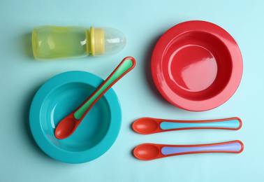 Set of colorful plastic dishware on light blue background, flat lay. Serving baby food