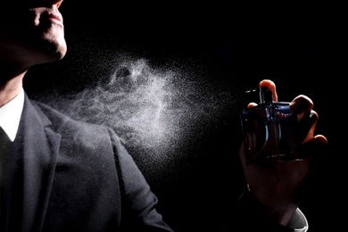 Man spraying luxury perfume on black background, closeup