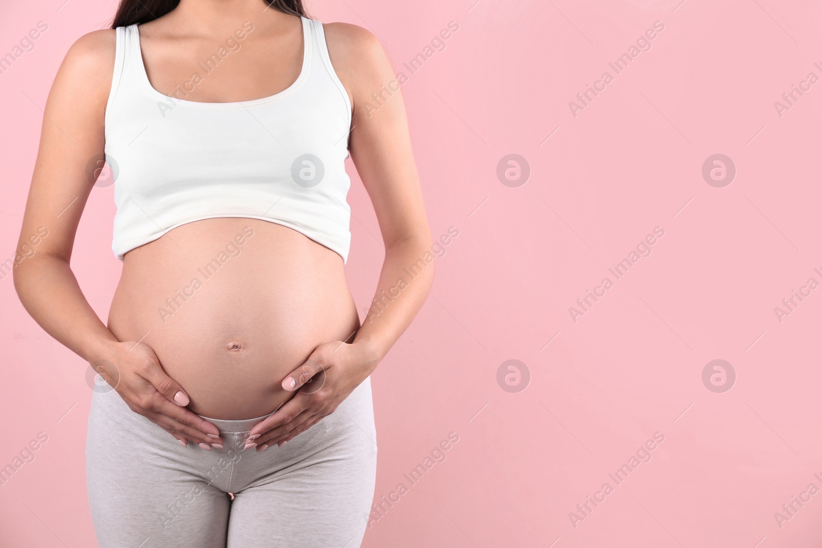 Photo of Young pregnant woman holding hands on belly against color background, closeup. Space for text