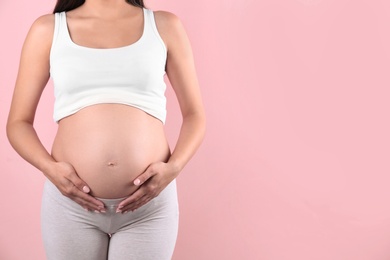 Young pregnant woman holding hands on belly against color background, closeup. Space for text