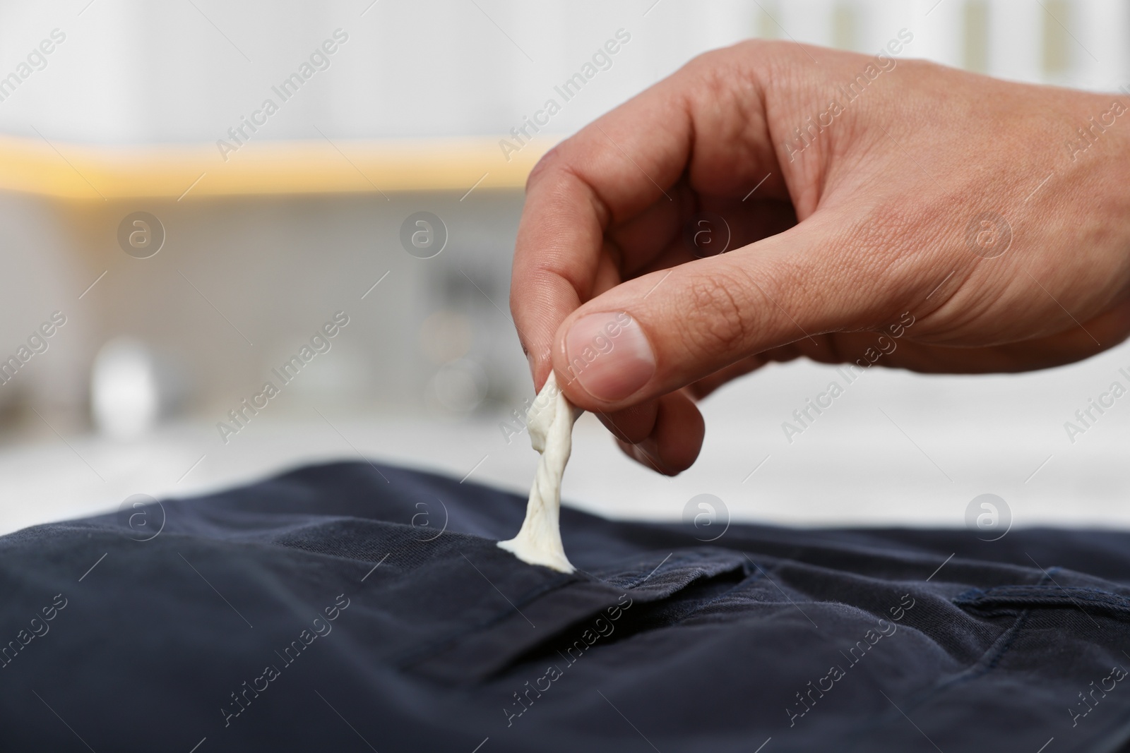 Photo of Man removing chewing gum from black jeans indoors, closeup. Space for text