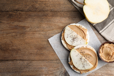 Photo of Puffed rice cakes with peanut butter and pear on wooden table, flat lay. Space for text