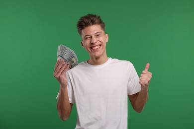 Happy man with dollar banknotes showing thumb up on green background