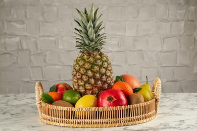 Photo of Fresh ripe fruits in wicker tray on white marble table