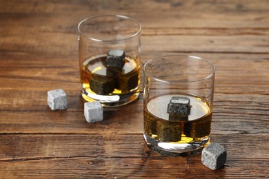 Whiskey stones and drink in glasses on wooden table, closeup