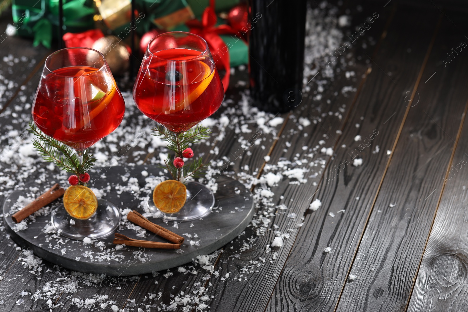 Photo of Christmas Sangria cocktail in glasses and snow on dark wooden table, space for text