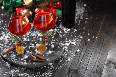 Photo of Christmas Sangria cocktail in glasses and snow on dark wooden table, space for text