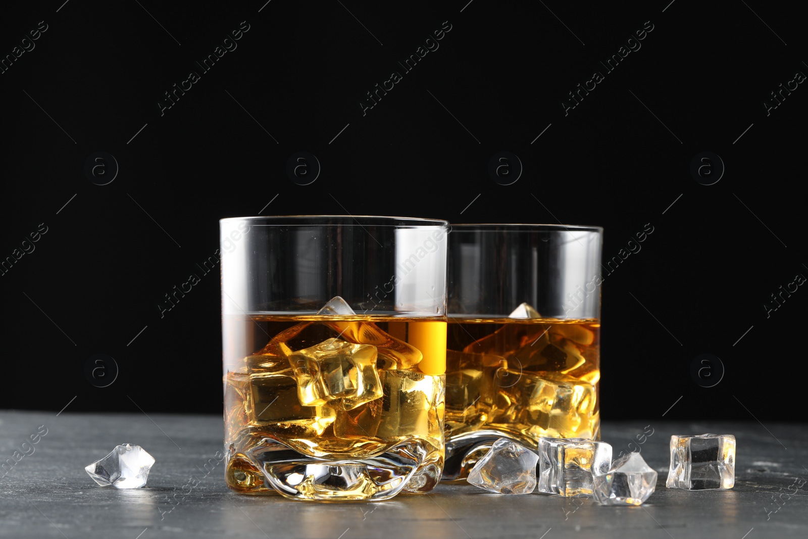 Photo of Whiskey and ice cubes in glasses on black table, closeup