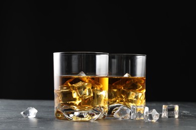 Photo of Whiskey and ice cubes in glasses on black table, closeup