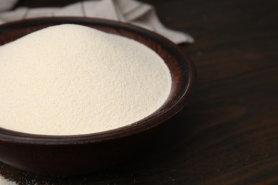 Photo of Uncooked organic semolina in bowl on wooden table, closeup. Space for text