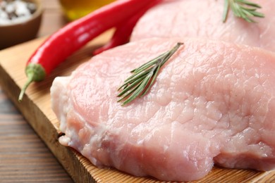 Pieces of raw pork meat, rosemary and chili peppers on wooden table, closeup