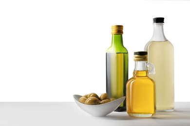 Photo of Bottles of different cooking oils and olives on white background, space for text