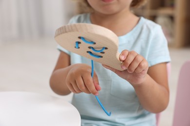 Motor skills development. Little girl playing with wooden lacing toy at table indoors, closeup