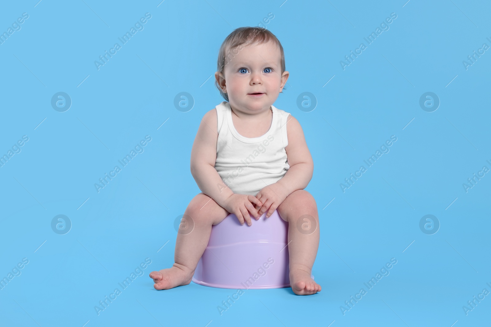 Photo of Little child sitting on baby potty against light blue background