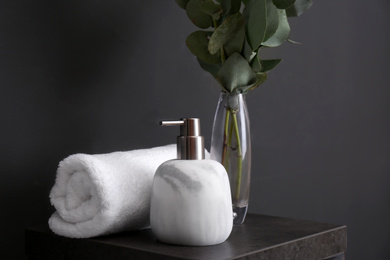 Photo of Clean soft towel and soap dispenser on stand near black wall