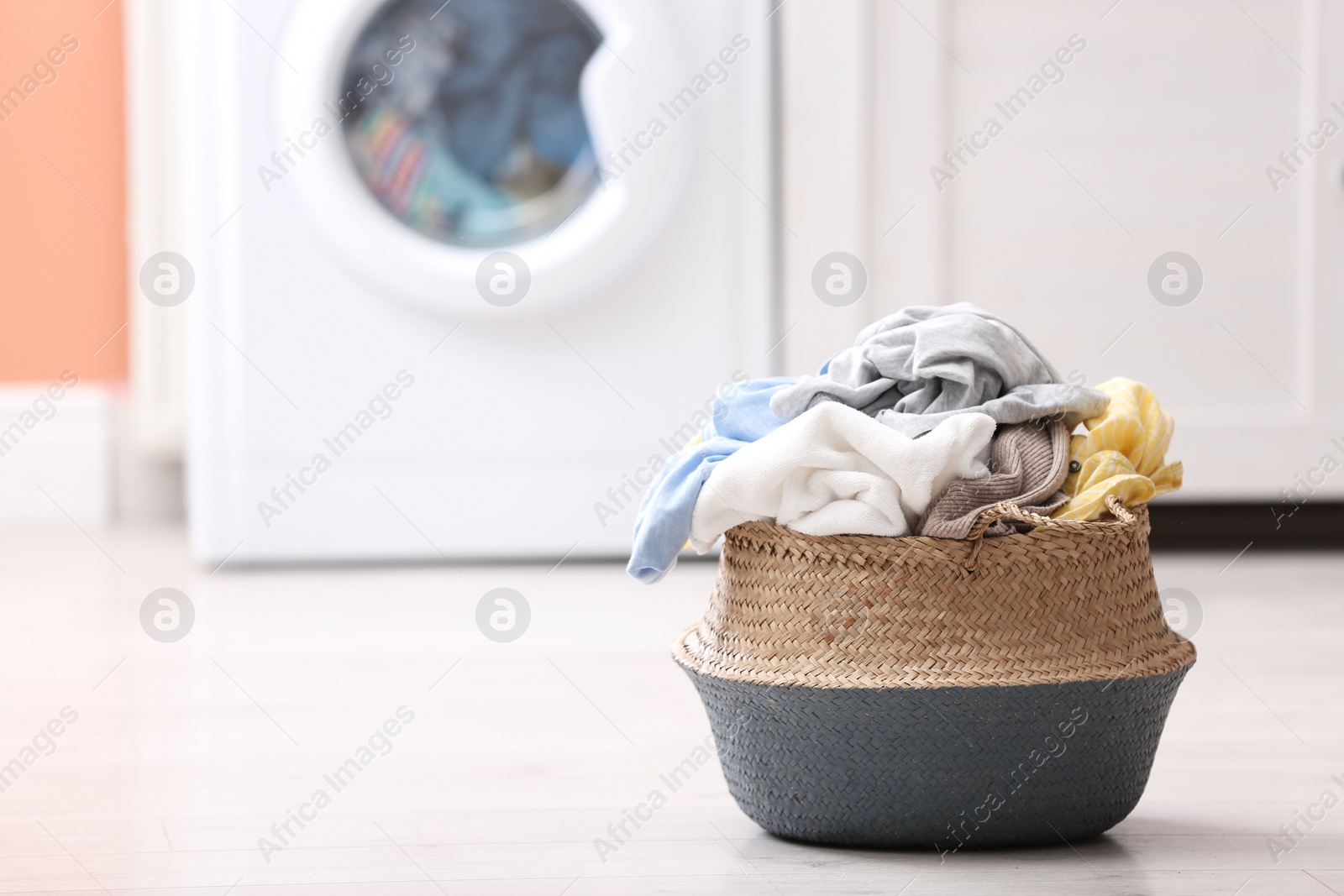 Photo of Wicker basket with dirty laundry on floor indoors, space for text