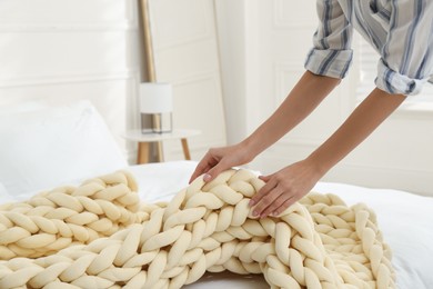 Photo of Woman folding chunky knit blanket at home, closeup