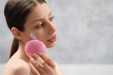 Young woman washing face with brush and cleansing foam indoors. Space for text
