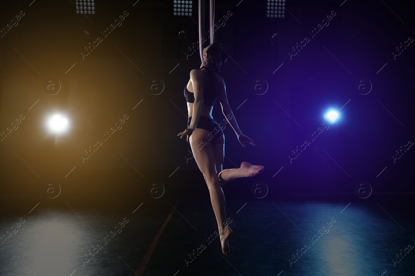 Photo of Young woman performing acrobatic element on aerial silk indoors