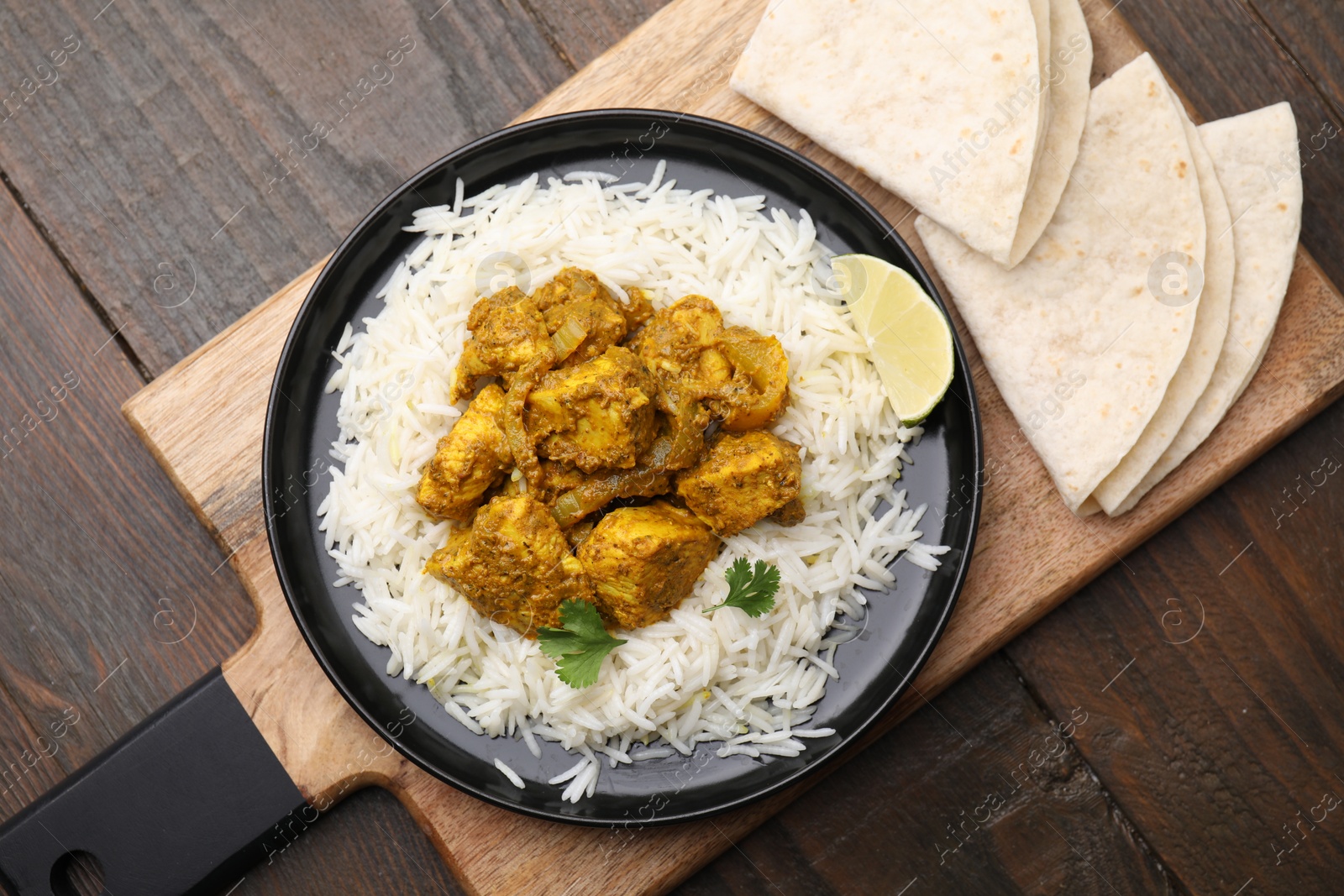 Photo of Delicious chicken curry with rice and tortillas on wooden table, top view