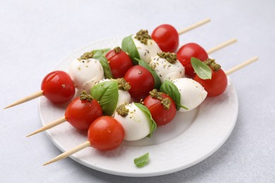 Photo of Caprese skewers with tomatoes, mozzarella balls, basil and pesto sauce on white table, closeup