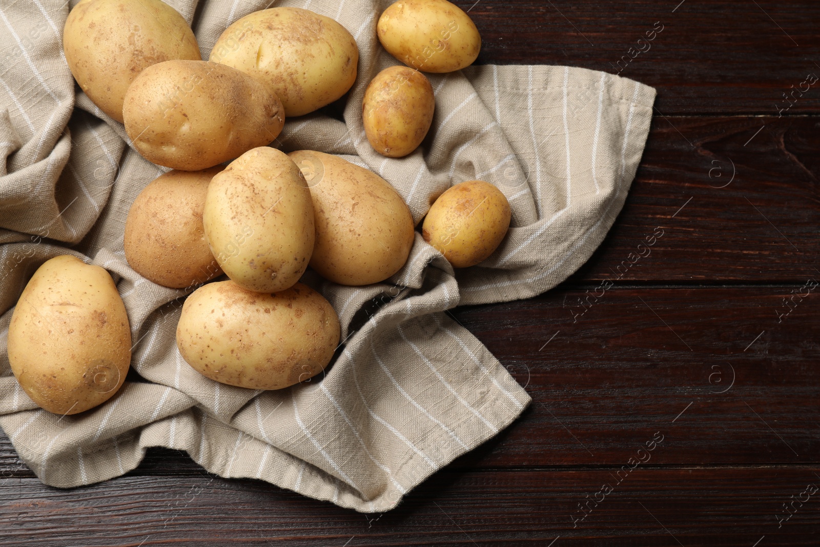 Photo of Raw fresh potatoes and napkin on wooden table. Space for text