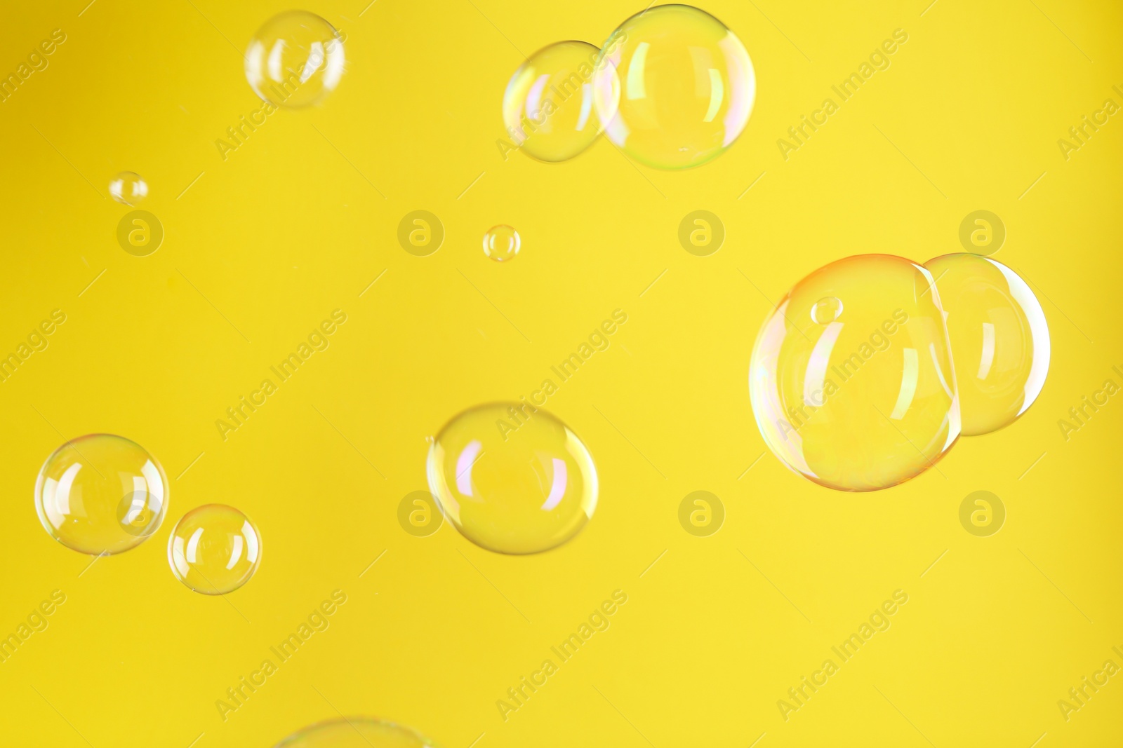 Photo of Beautiful transparent soap bubbles on yellow background