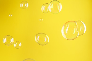 Photo of Beautiful transparent soap bubbles on yellow background