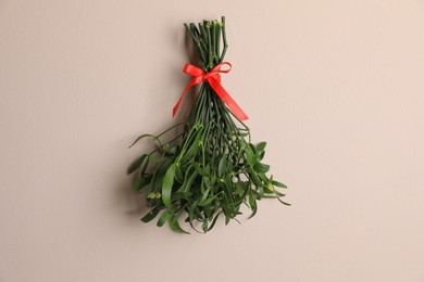 Photo of Mistletoe bunch with red bow on beige table, top view. Traditional Christmas decor