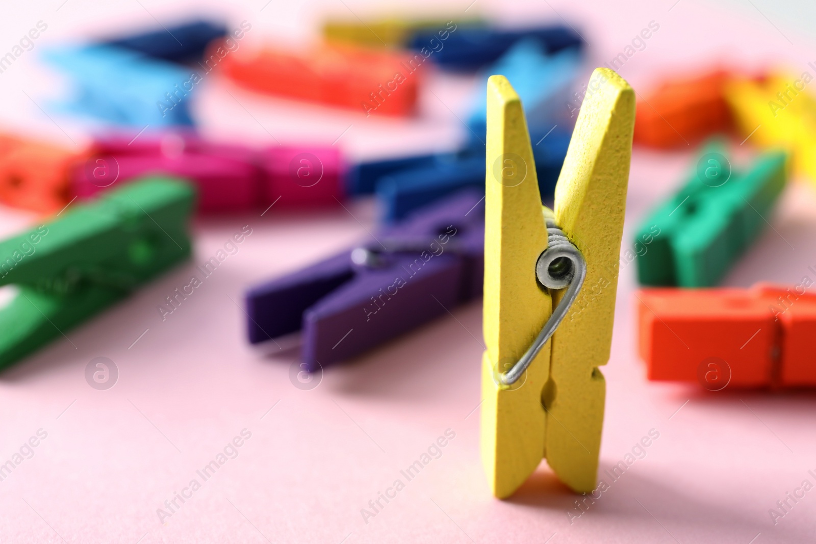 Photo of Yellow clothespin standing among lying ones on pink background. Diversity concept