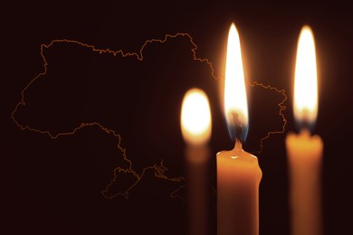 Image of Burning candles and outline map of Ukraine on dark background, closeup