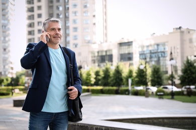 Portrait of handsome mature man talking on phone in city center. Space for text