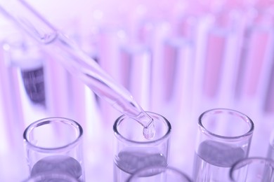 Dripping liquid from pipette into test tube on violet background, closeup