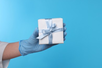 Photo of Doctor holding gift box on light blue background, closeup. Medical present