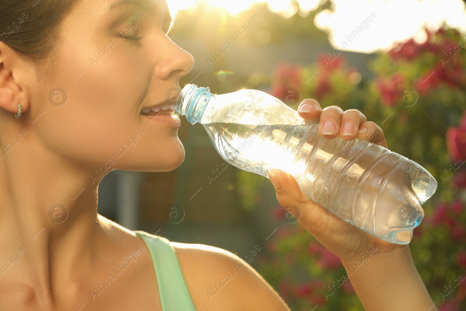 Photo of Happy young woman drinking water outdoors on hot summer day, closeup. Refreshing drink