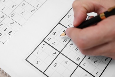 Man writing numbers in sudoku puzzle grid, closeup