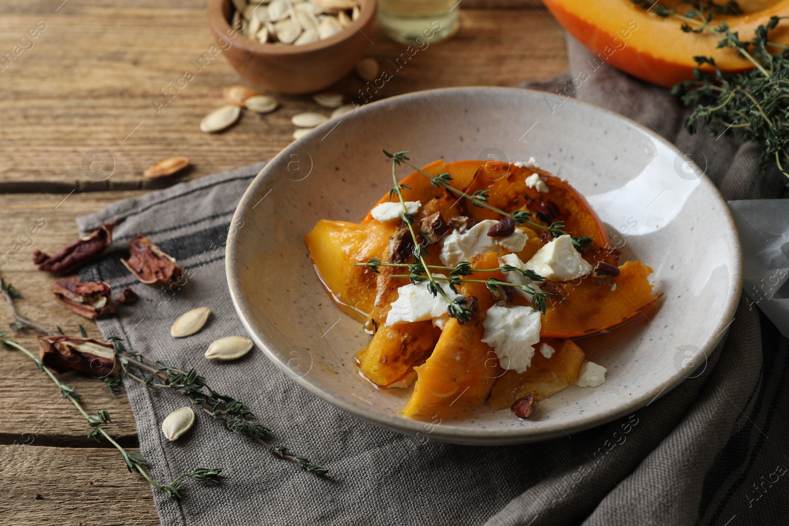 Photo of Baked pumpkin slices served with cheese, thyme and pecans on wooden table, closeup